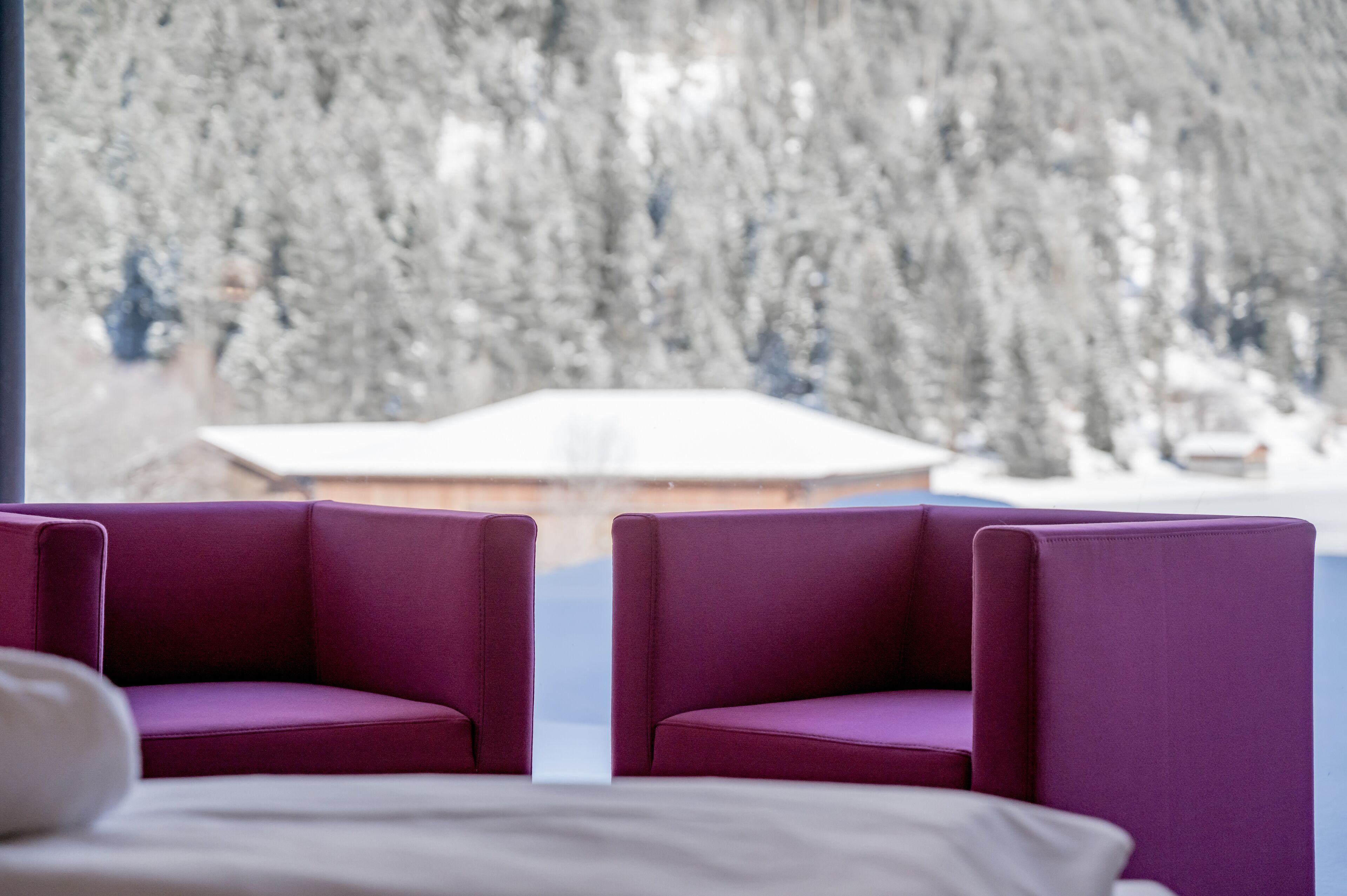 Ein Zimmer mit zwei violetten Sesseln und Blick auf eine verschneite Landschaft.