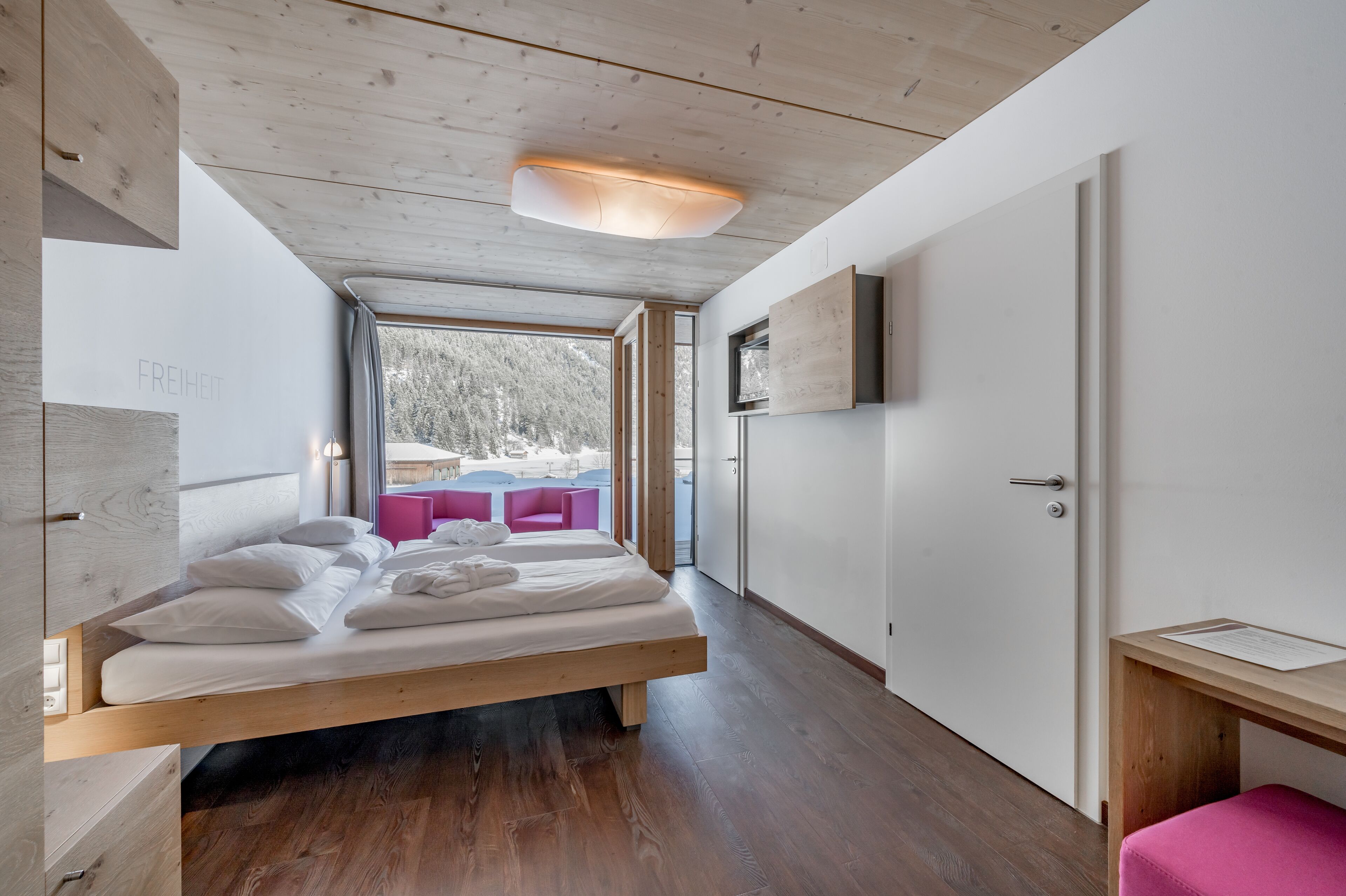 Un dormitorio moderno con una cama de madera, un escritorio y vistas a una zona de estar exterior.