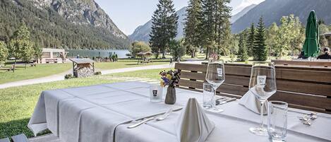 A table set outdoors with a mountain view, a bench, and a small table with a candle and flowers.