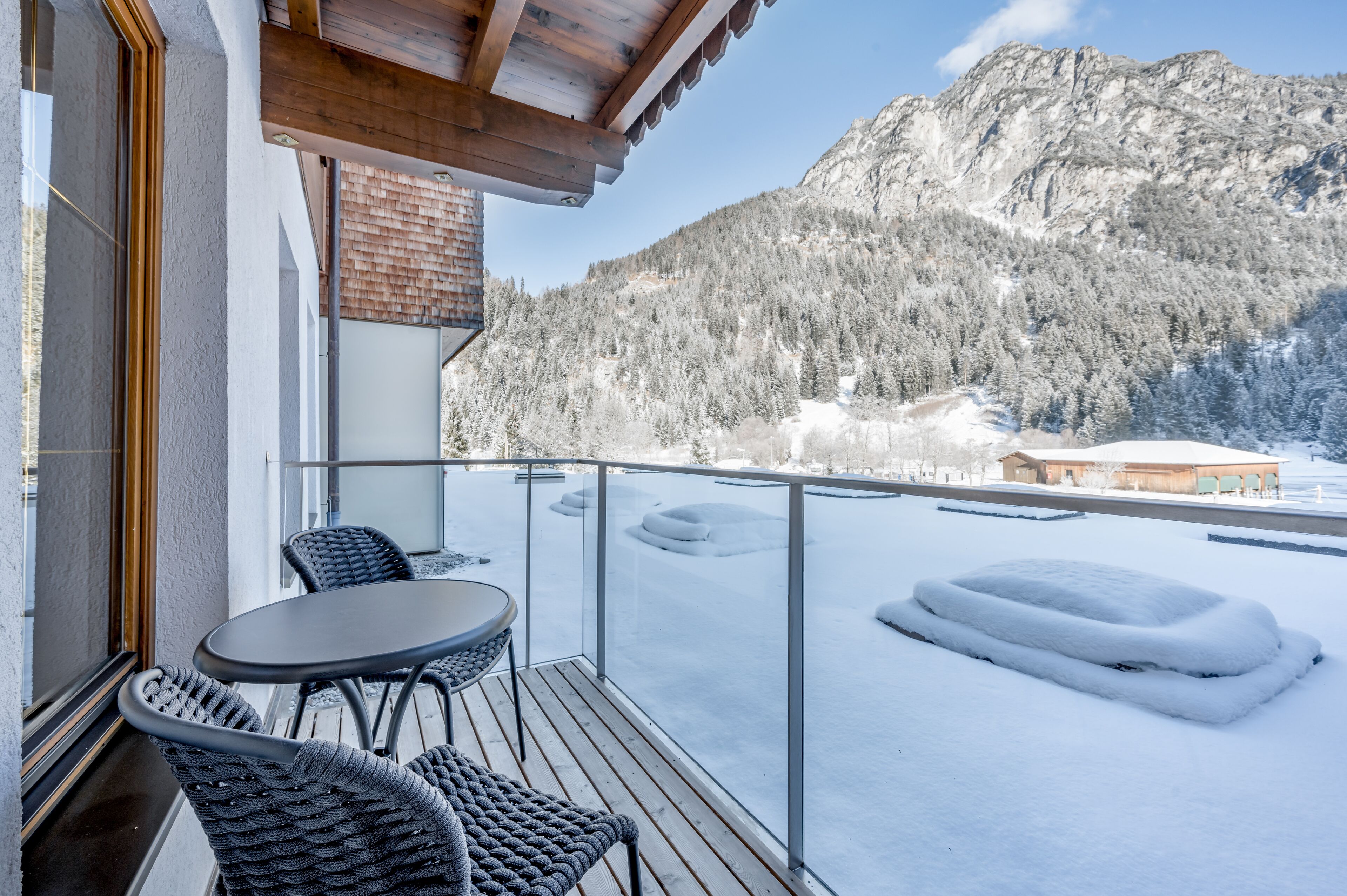 A balcony with a table and chairs, overlooking a snowy mountain landscape.