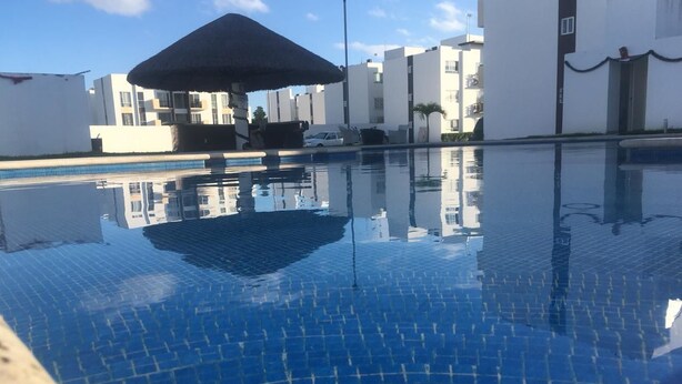 A swimming pool with a tiled floor and a thatched umbrella structure. - Apartamento Vacacional (Playa del Carmen)