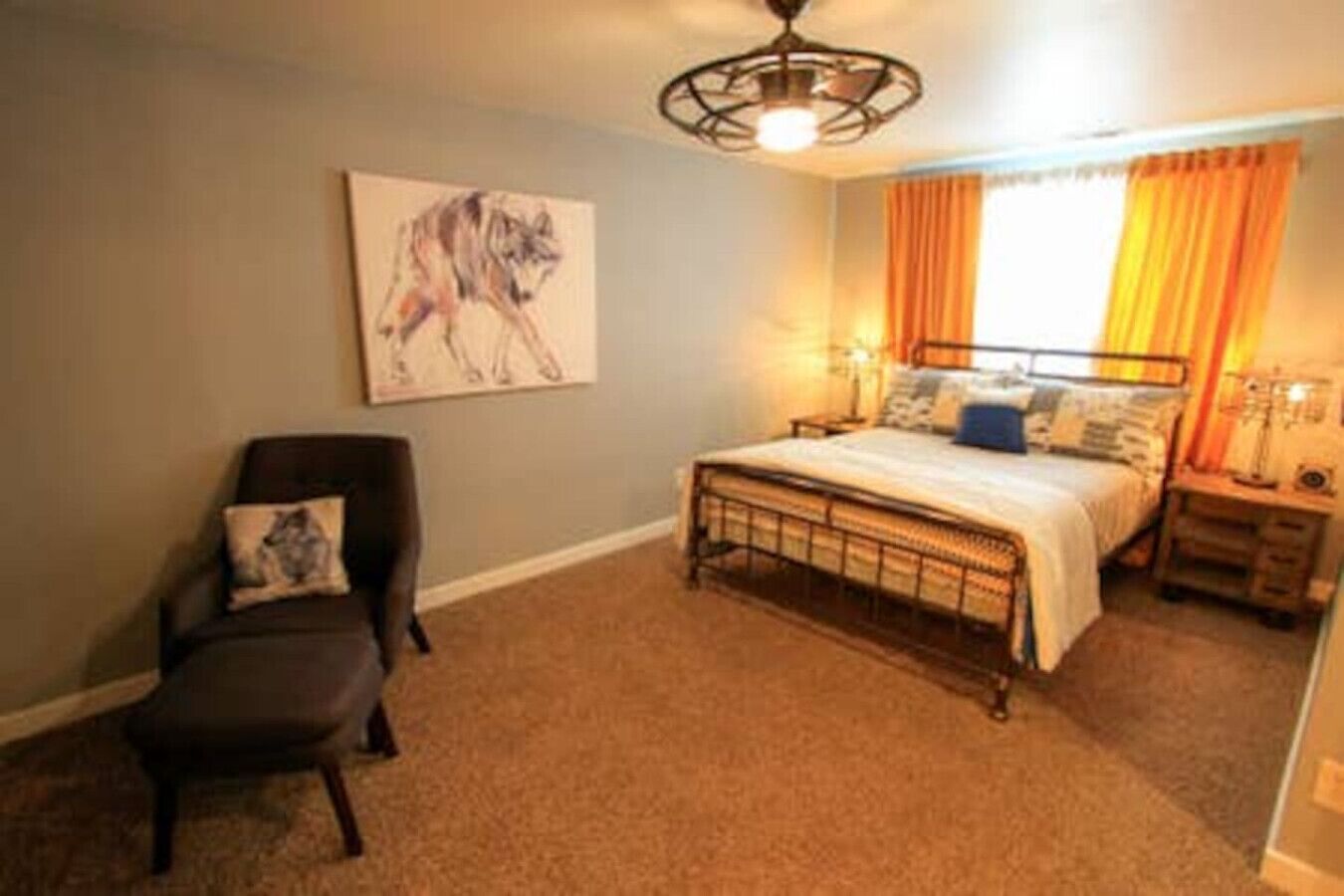 Un dormitorio con cama, una silla, una mesita de noche, una lámpara y un cuadro en la pared.