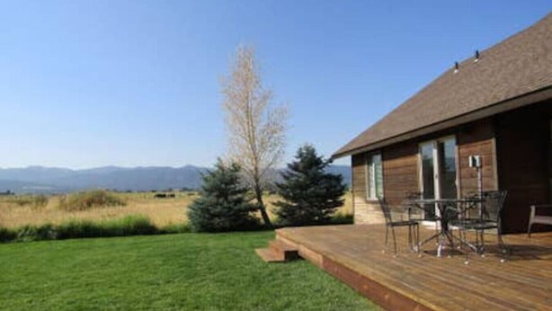 Eine Holzterrasse mit Gartenmöbeln, einer Rasenfläche und Blick auf Berge im Hintergrund.