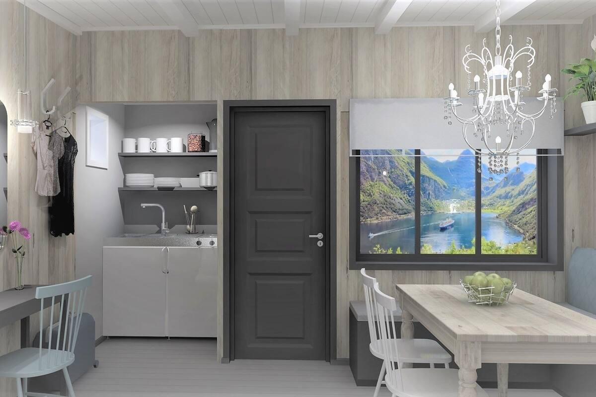 A modern kitchen with a grey door, a dining table with chairs, a chandelier, and a window with a scenic view.