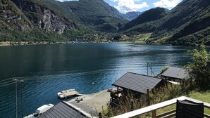 A lakeside view with a dock, a small boat, and a cabin with a sloped roof.