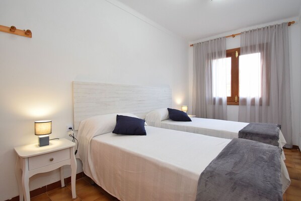 Una habitación de hotel con dos camas individuales, una mesita de noche con lámpara y una ventana con cortinas.