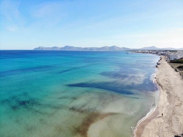 A coastal beach with clear water and a distant mountain range.