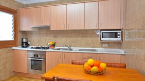 A kitchen with wooden cabinets, a microwave, a stove, and a dining table with a fruit basket.