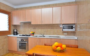 Una cocina con armarios de madera, microondas, estufa y una mesa de comedor con una cesta de frutas.