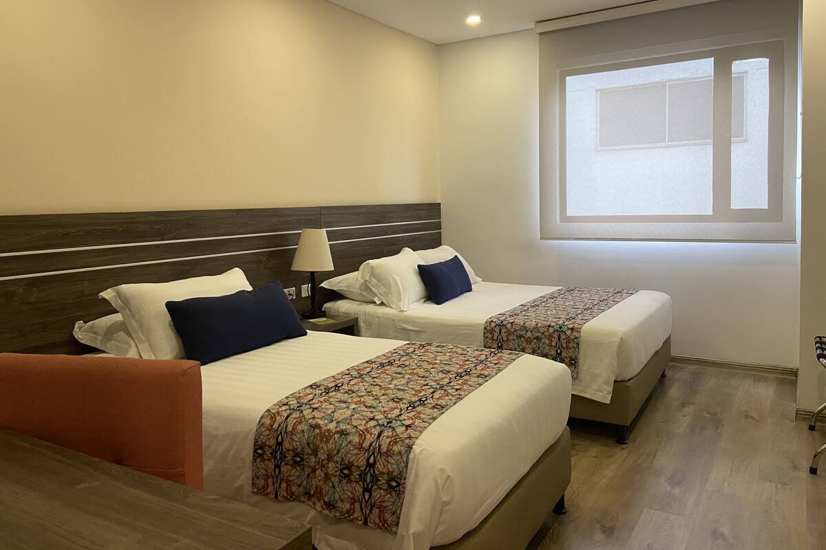 Quarto de hotel com duas camas, uma janela e piso de madeira.