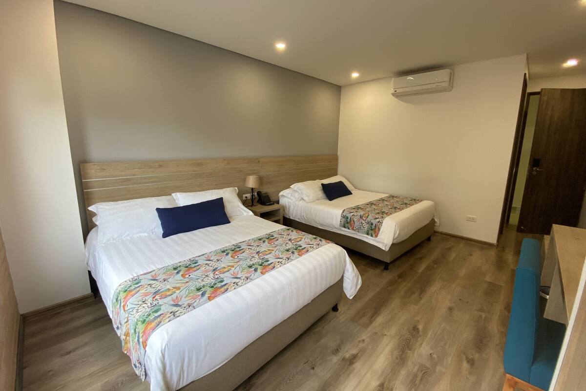 Une chambre d’hôtel avec deux lits, une tête de lit en bois, une table de chevet avec une lampe et une chaise bleue.
