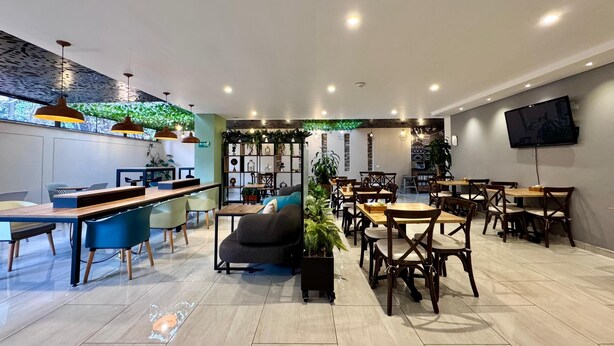 A modern cafe with a mix of seating options, including tables and chairs, and a large screen mounted on the wall. - EcoHub Hotel Medellin (Medellín)