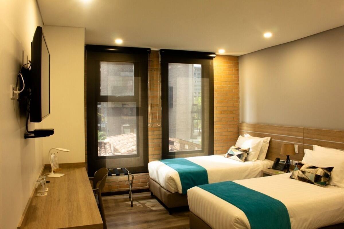 Une chambre d’hôtel avec deux lits, un bureau, une chaise, une télévision et une fenêtre donnant sur un paysage agréable.