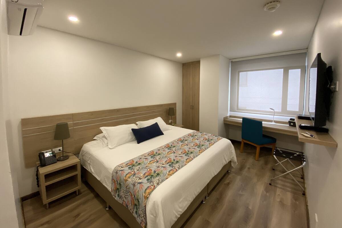 Une chambre d’hôtel avec un lit, une table de chevet, une lampe, une chaise, un bureau et une fenêtre.