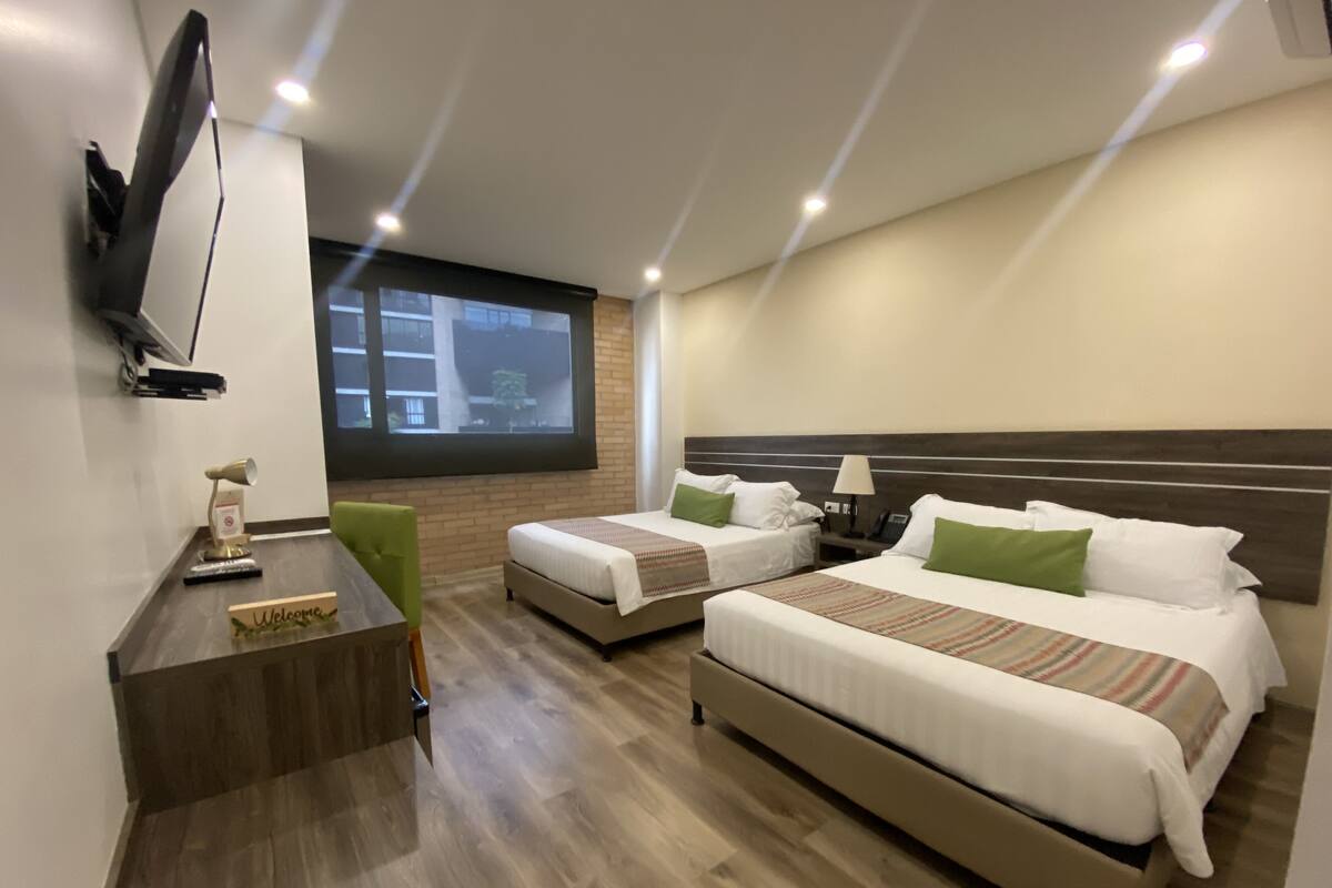 Une chambre d’hôtel avec deux lits, un bureau, un téléviseur fixé au mur et une fenêtre donnant sur la ville.