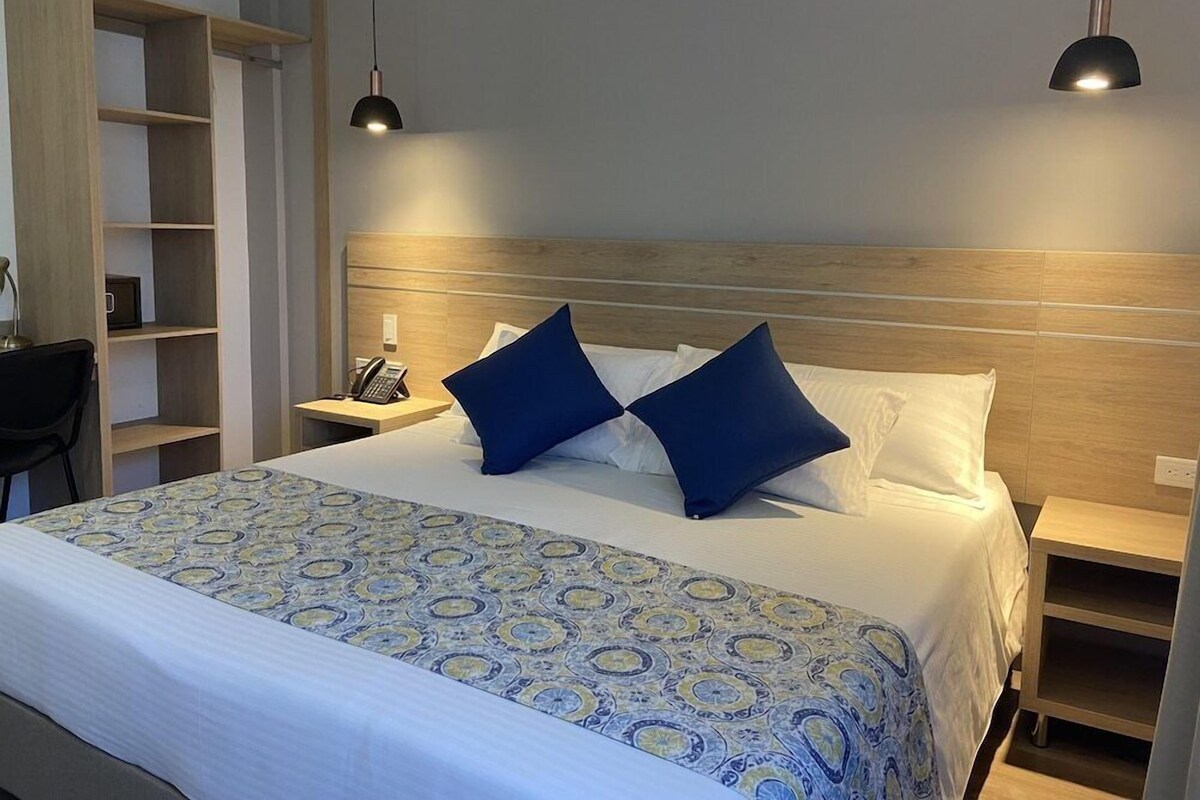 Ein Hotelzimmer mit einem großen Bett, zwei Nachttischen, einem Schreibtisch, einem Stuhl und einem Kleiderschrank.