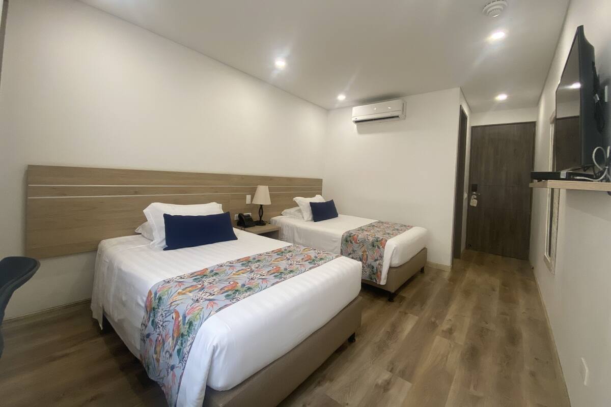 Une chambre d’hôtel avec deux lits, un bureau, une chaise, un appareil de climatisation et un téléviseur.