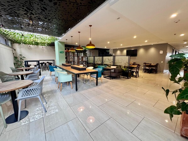 A modern cafe with a variety of seating options including tables and chairs, a central island with seating, and a ceiling with hanging lights. - EcoHub Hotel Medellin (Medellín)
