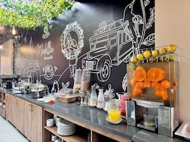 Bar de pequeno-almoço com diversos alimentos e parede de lousa com desenhos.