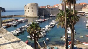 A coastal town with a historic stone tower, a marina with boats, and a palm tree. - Apartment Sendi - Near the beach, fully equipped (Dubrovnik)