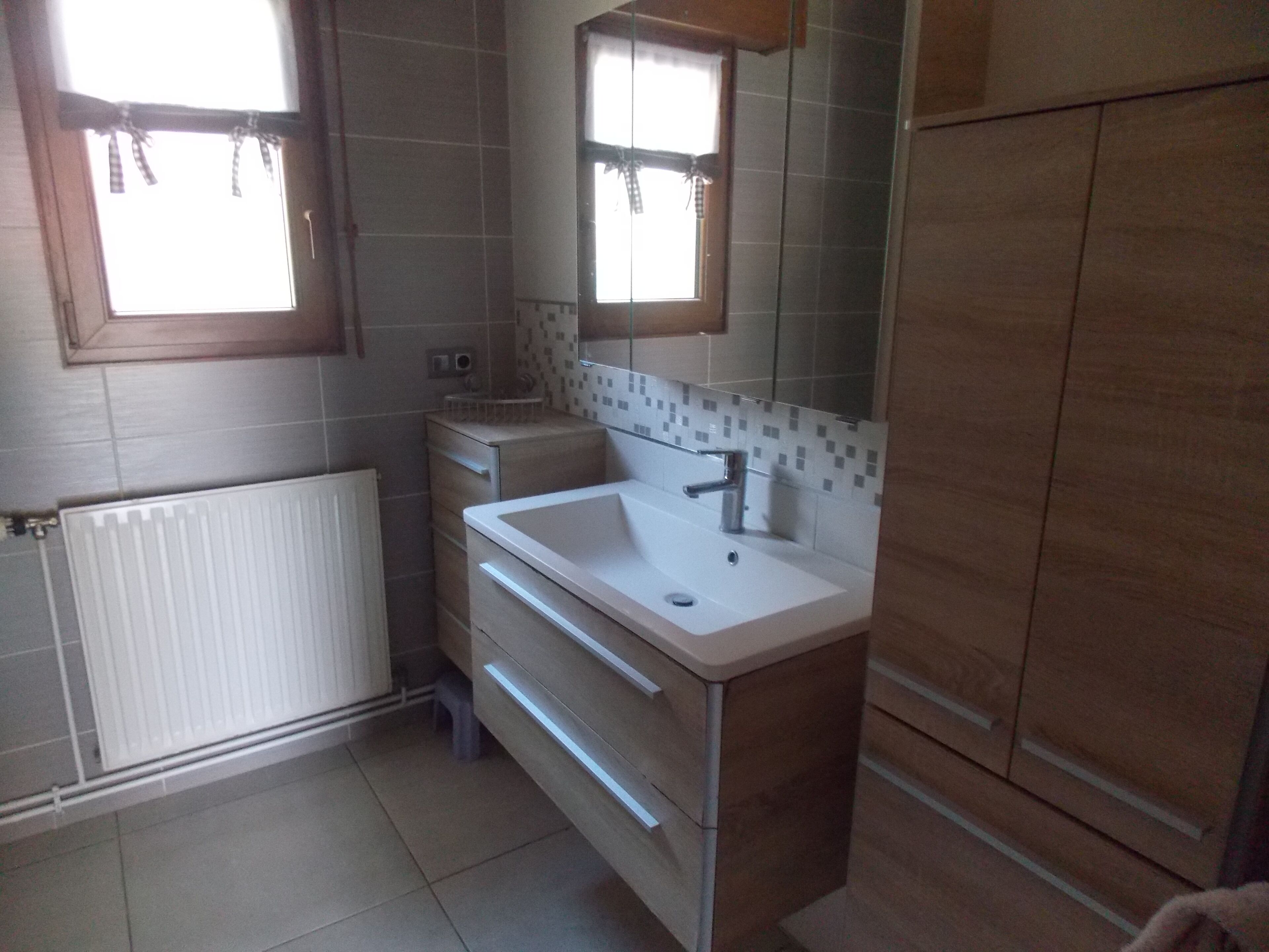 A bathroom with a white sink, wooden cabinet, and a window with curtains.