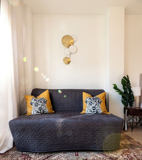 Un salon avec un canapé gris foncé, deux coussins de couleur jaune moutarde et un élément décoratif mural.