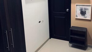Une pièce avec une armoire en bois sombre, une porte noire, un téléviseur fixé au mur et une petite étagère sur laquelle est posée une citation inspirante encadrée.