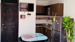 Une cuisine compacte avec une porte en bois foncé, un téléviseur à écran plat, un réfrigérateur et une table à manger avec des chaises.