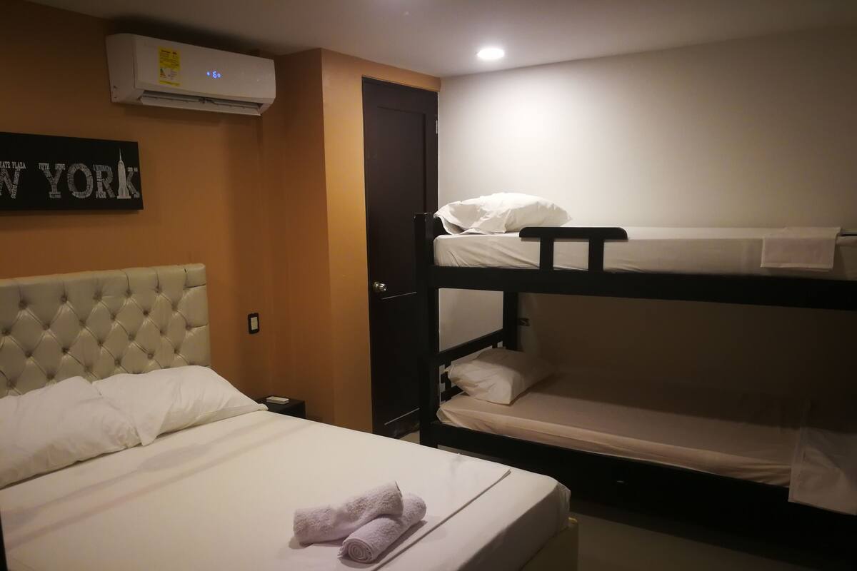 A hotel room with a single bed, a bunk bed, a wall-mounted air conditioner, and a sign with the text "NEW YORK".
