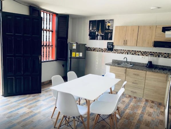 Una cocina compacta con una mesa y sillas blancas, un refrigerador y un lavamanos.