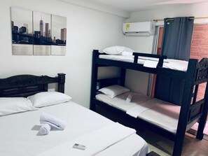 Una habitación con literas, una cama individual y un cuadro de un paisaje urbano en la pared.