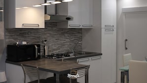 Una cocina moderna con microondas, estufa y lavabo. Hay dos sillas y una pequeña mesa.