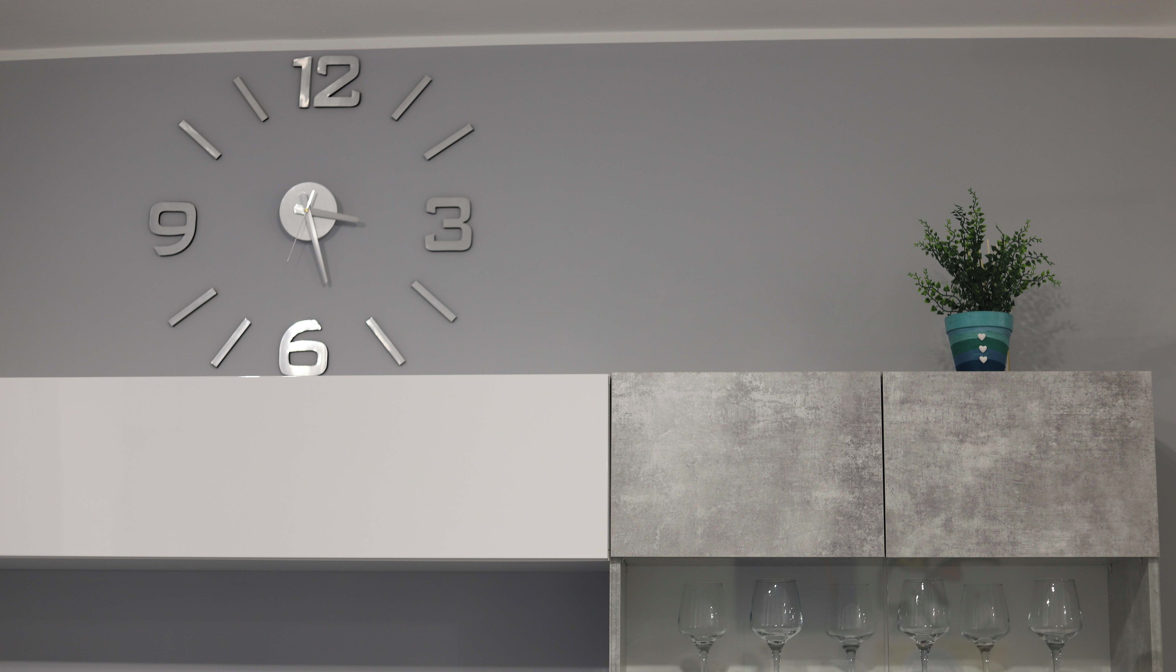 Ein modernes Wohnzimmer mit einer großen Wanduhr, einer Topfpflanze und einer Weinflaschenpräsentation.