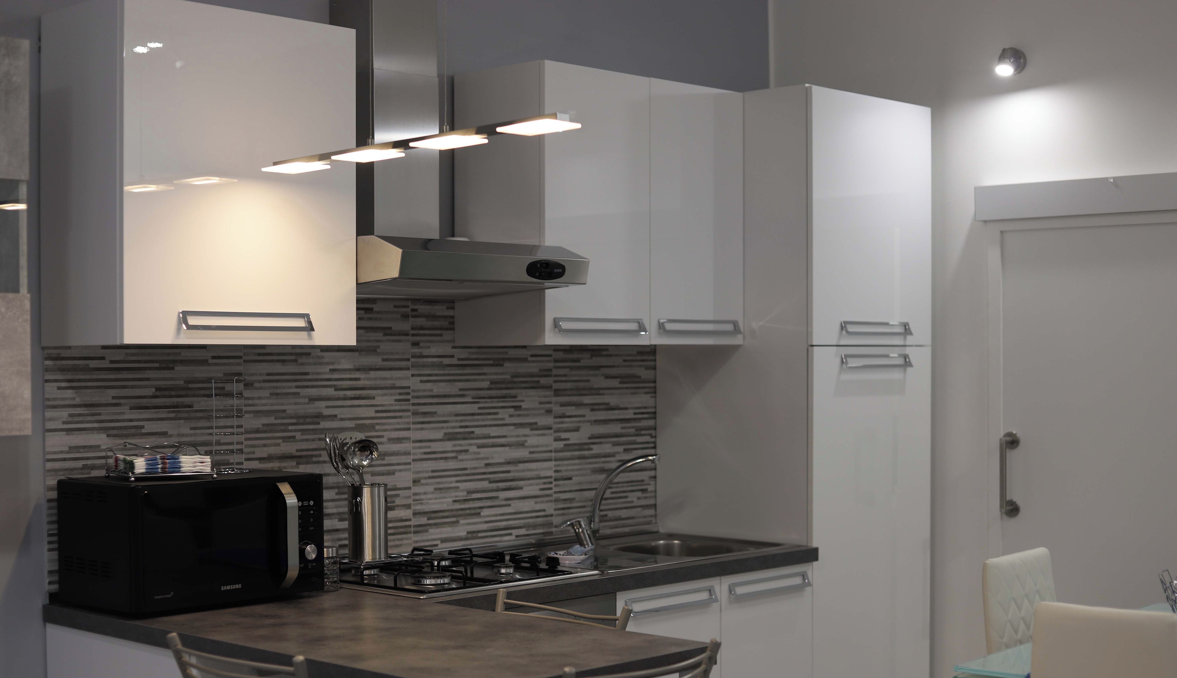 A modern kitchen with a microwave, stove, and sink. There are two chairs and a small table.