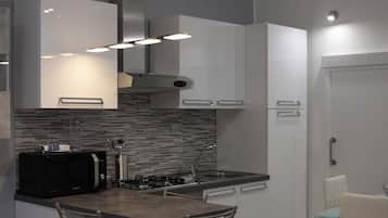 A modern kitchen with a microwave, stove, and sink. There are two chairs and a small table.