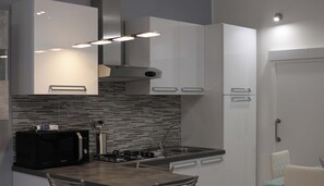 Una cocina moderna con microondas, estufa y lavabo. Hay dos sillas y una pequeña mesa.