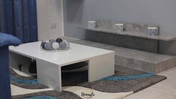 A modern living room with a white coffee table, a grey sofa, and a patterned rug.