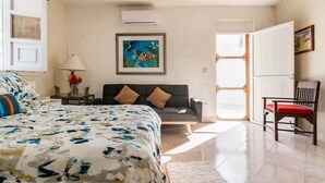A bedroom with a bed, a sofa, a chair, a painting, and a window. - Cozy Studio/Room Enclosed on an Oceanfront Property at Mima´s Village Cozumel (San Miguel de Cozumel)