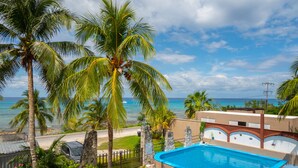 A pool area with a view of the ocean, surrounded by palm trees and a building with a pool. - Cozy Studio/Room Enclosed on an Oceanfront Property at Mima´s Village Cozumel (San Miguel de Cozumel)