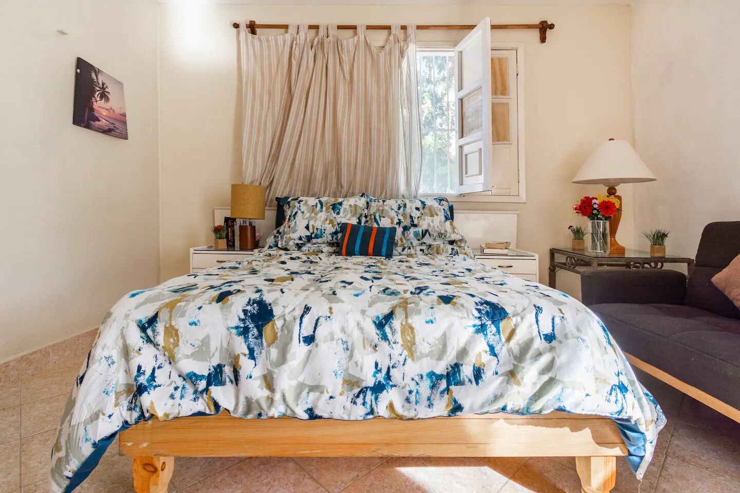 A bedroom with a bed, a bedside table, a lamp, and a view of the outdoors.