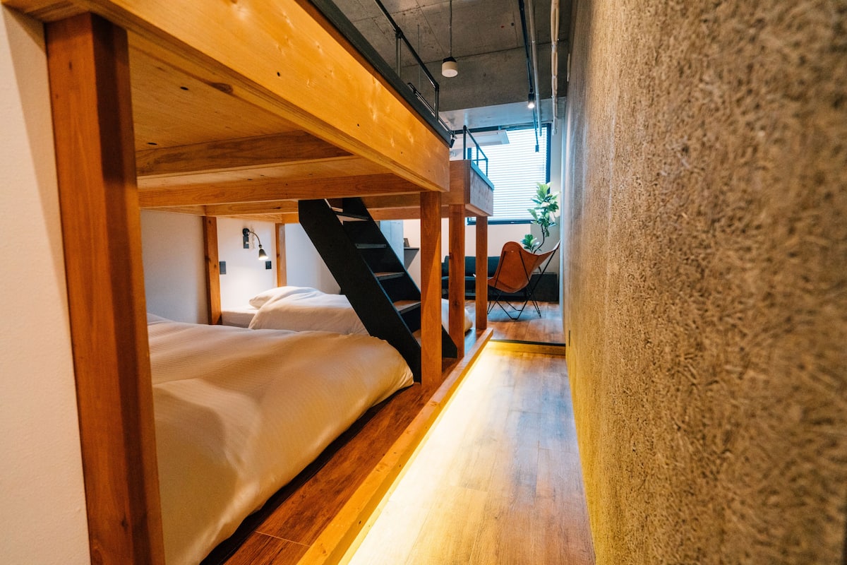 A narrow corridor with wooden flooring and a staircase leading to a room with a bed and a chair.