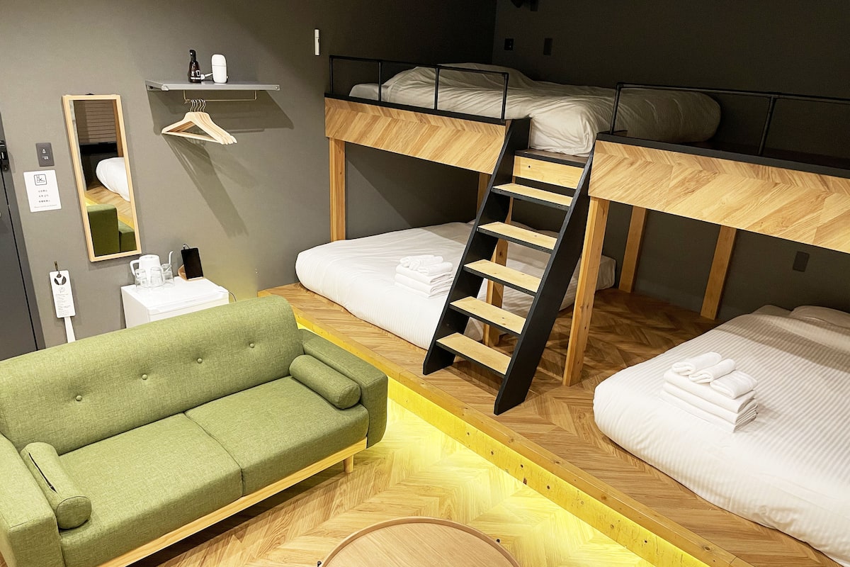 A room with bunk beds, a green sofa, and a wooden ladder.