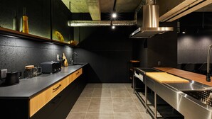 A modern kitchen with a long countertop, stainless steel appliances, and a wooden cabinet. - ZONK HOTEL NAKASU-DEAIBASHI (Fukuoka)