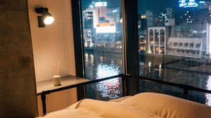 A hotel room with a bed, a nightstand with a lamp, and a view of a cityscape through a window. - ZONK HOTEL NAKASU-DEAIBASHI (Fukuoka)
