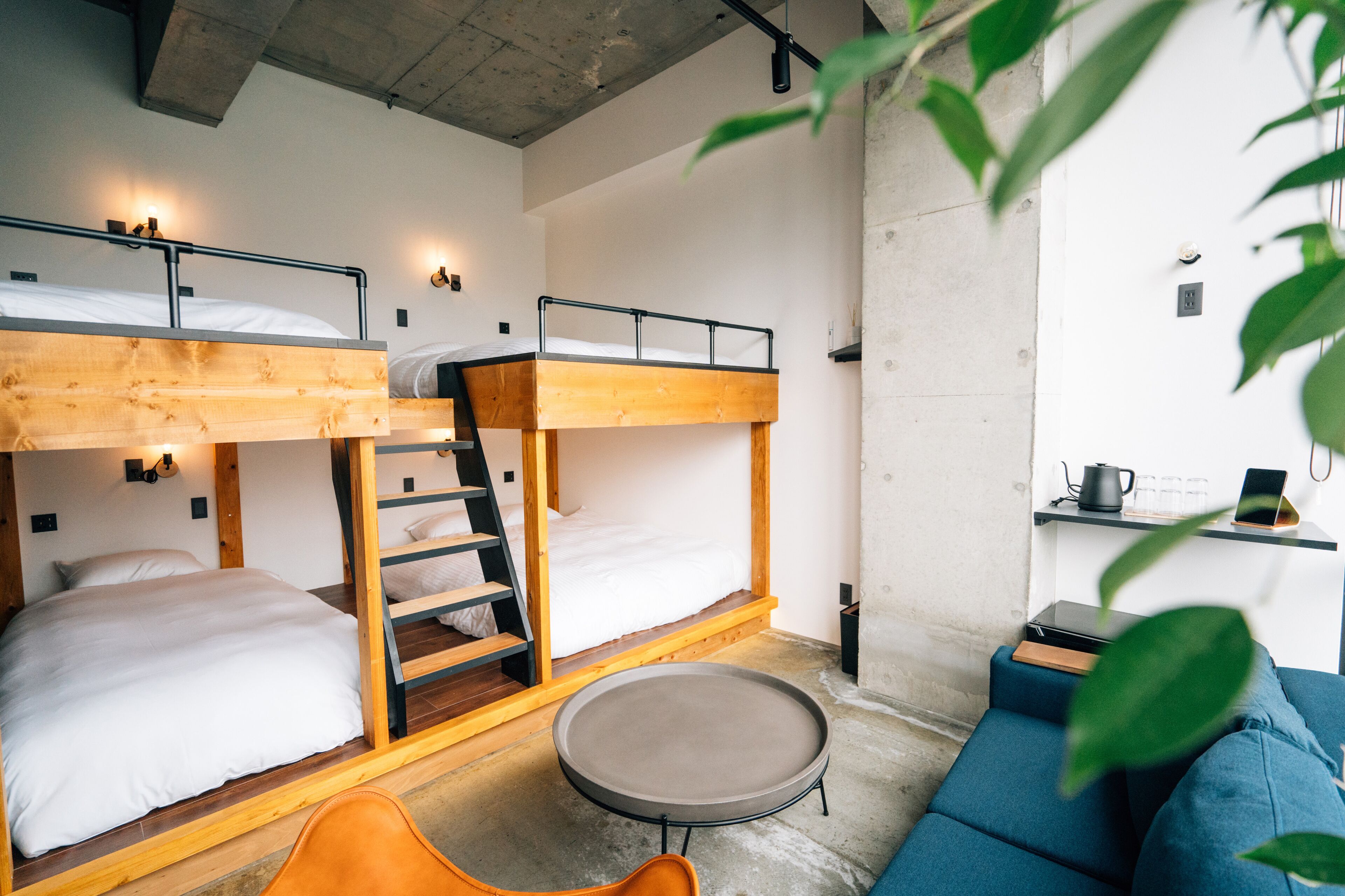 A bunk bed room with a small round table and a blue sofa.