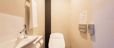A bathroom with a white sink, a towel hanging on a rack, a toilet, and a wall-mounted control panel.