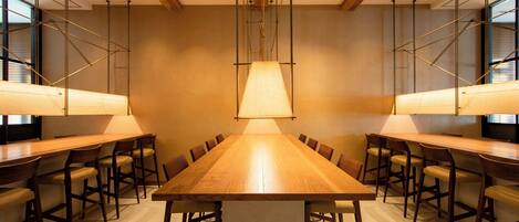 A conference room with a long wooden table, multiple chairs, and pendant lighting.