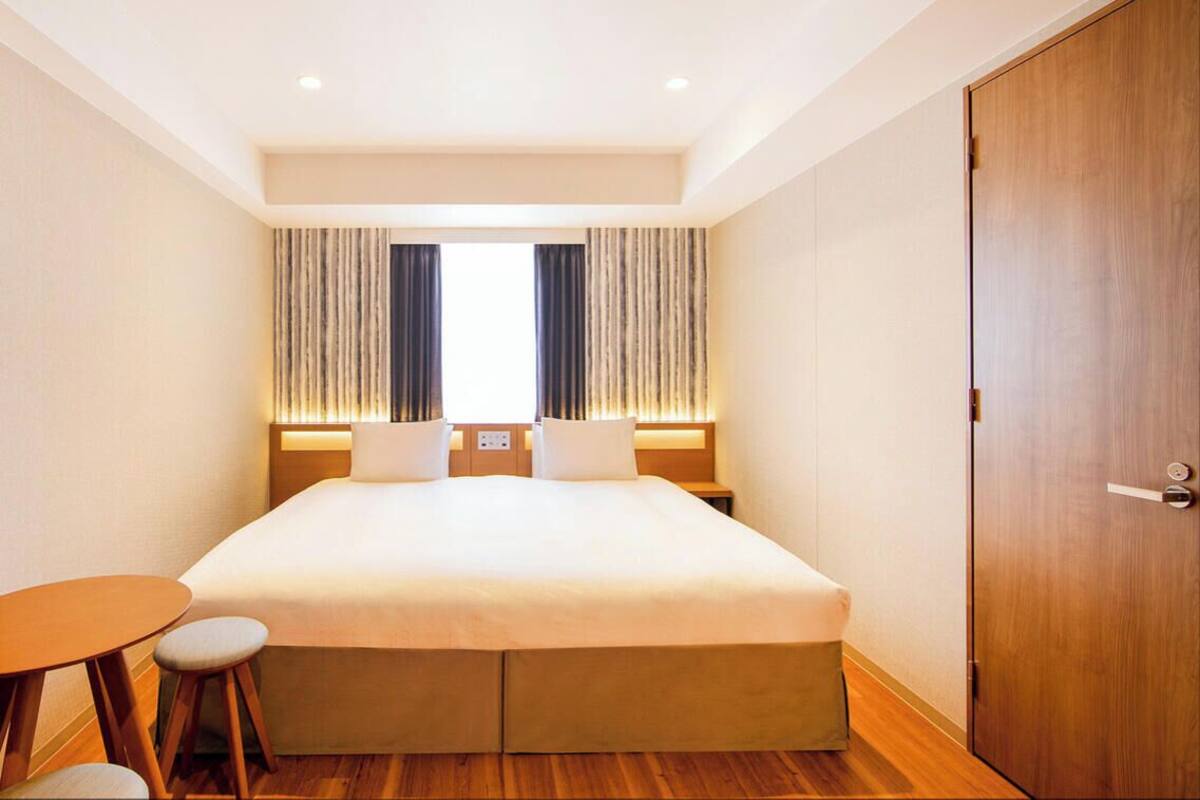 Una habitación de hotel con una cama grande, una mesita redonda pequeña y una puerta de madera.