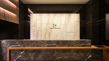 A reception desk with a marble top and a wooden bench. The wall behind the desk has a logo and the text "karaksa hotel grande".