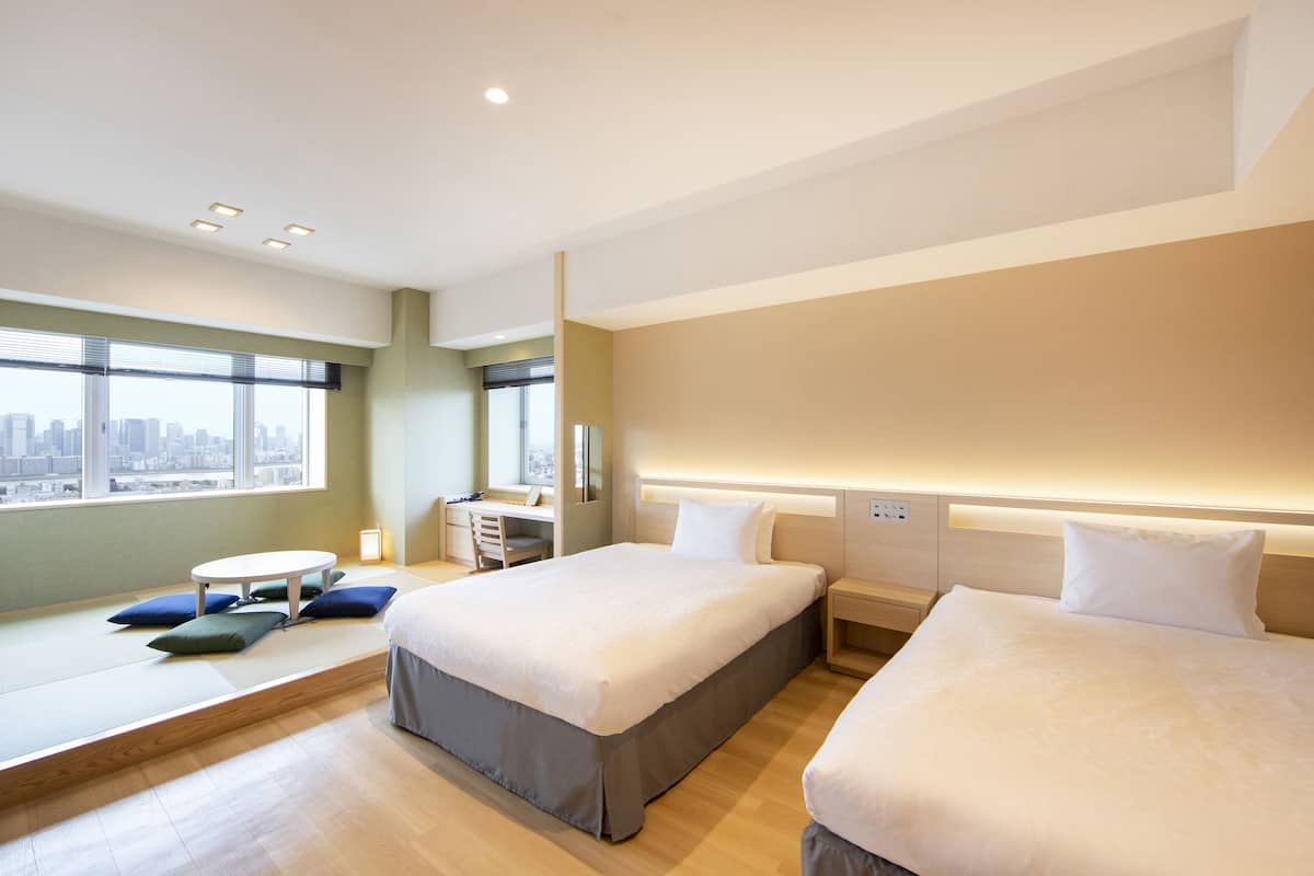 A modern hotel room with two beds, a desk, and a view of the city.
